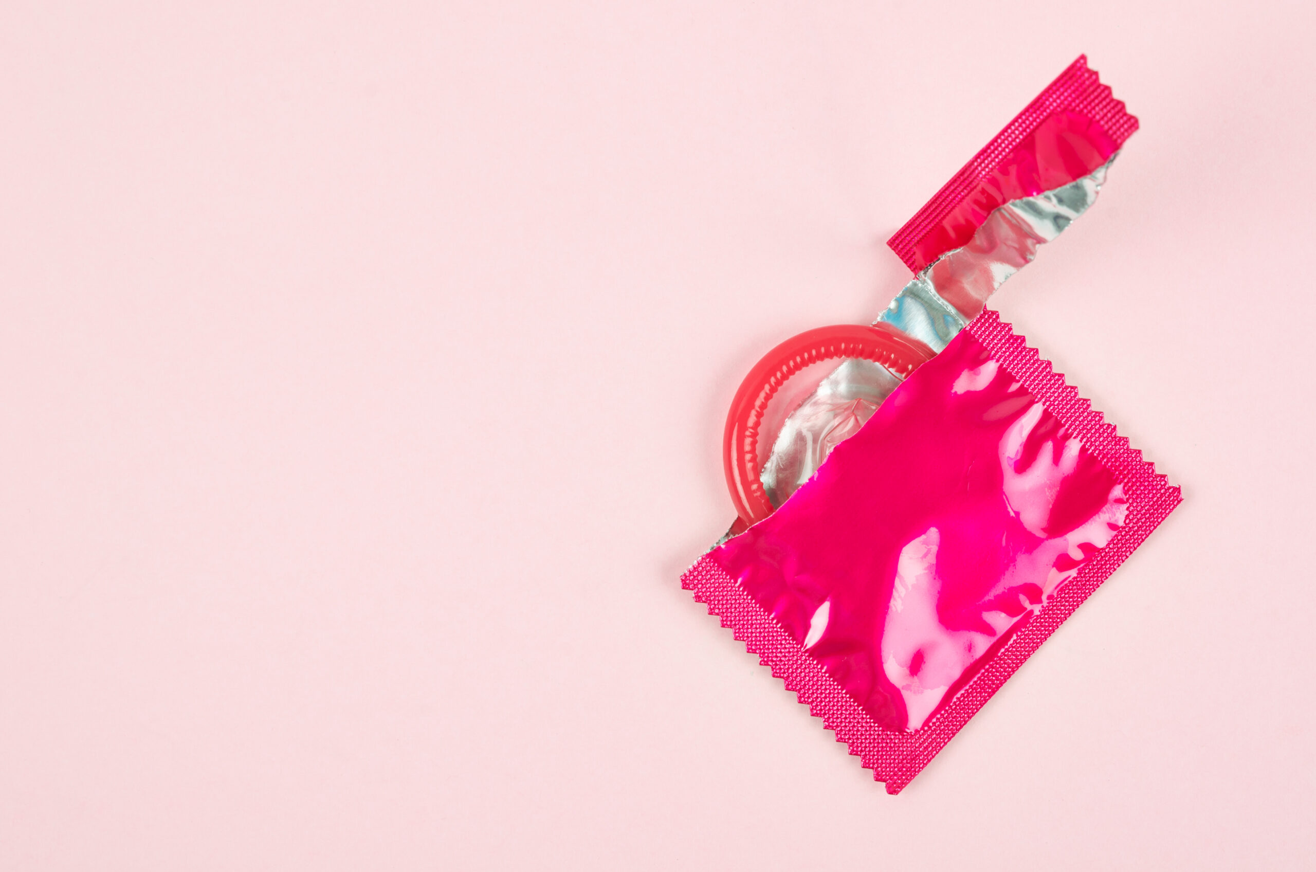 Pink opened condom unpack on a pink background.