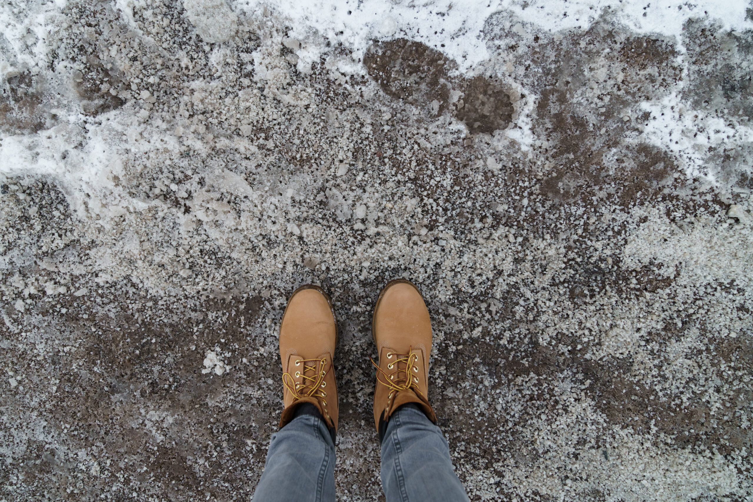 Anti-icing chemicals in winter season. Top view of winter boots and road strewn with technical salt or reagents to prevent icing. Effective tool to fight ice on surfaces